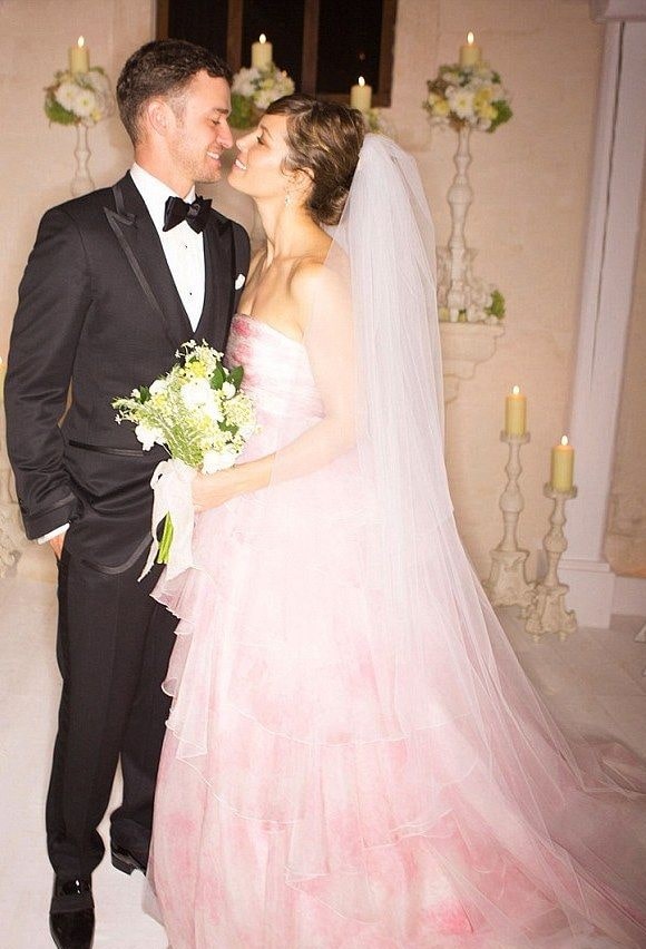 Jessica Biel and Justine Timberlake facing each and smiling while Jessica on her pinkish-white gown catching a bouquet and Justine in a Tuxedo.